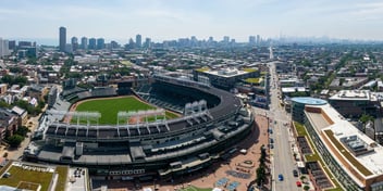Aerial view of Wrigley Field in Chicago, with the city skyline and Lake Michigan visible in the background.