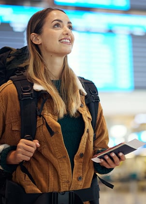 A female traveler with passport in hand looking at a flight schedule in an airport.