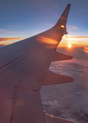 A view out of the window of plane with the sun setting just behind the wing.