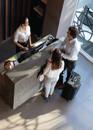 Aerial view of hotel reception desk with staff helping guests with luggage in bright lobby.