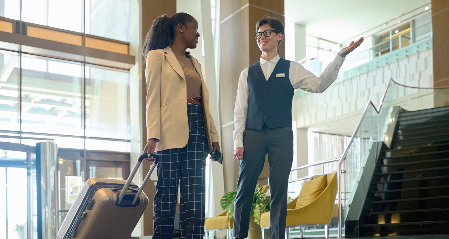 Young smiling manager of modern hotel consulting female traveler with suitcase entering lounge