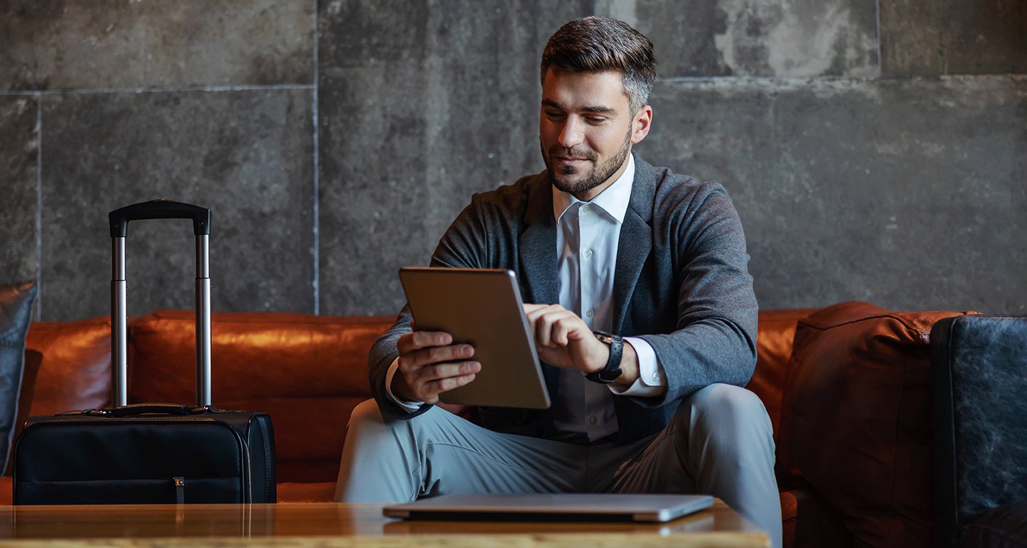 Businessman sitting on a couch in a hotel lobby using a tablet.