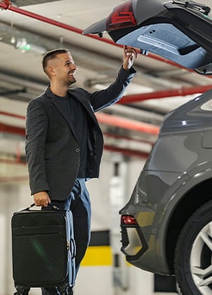 Smiling businessman is putting his luggage into a trunk and preparing for business travel.